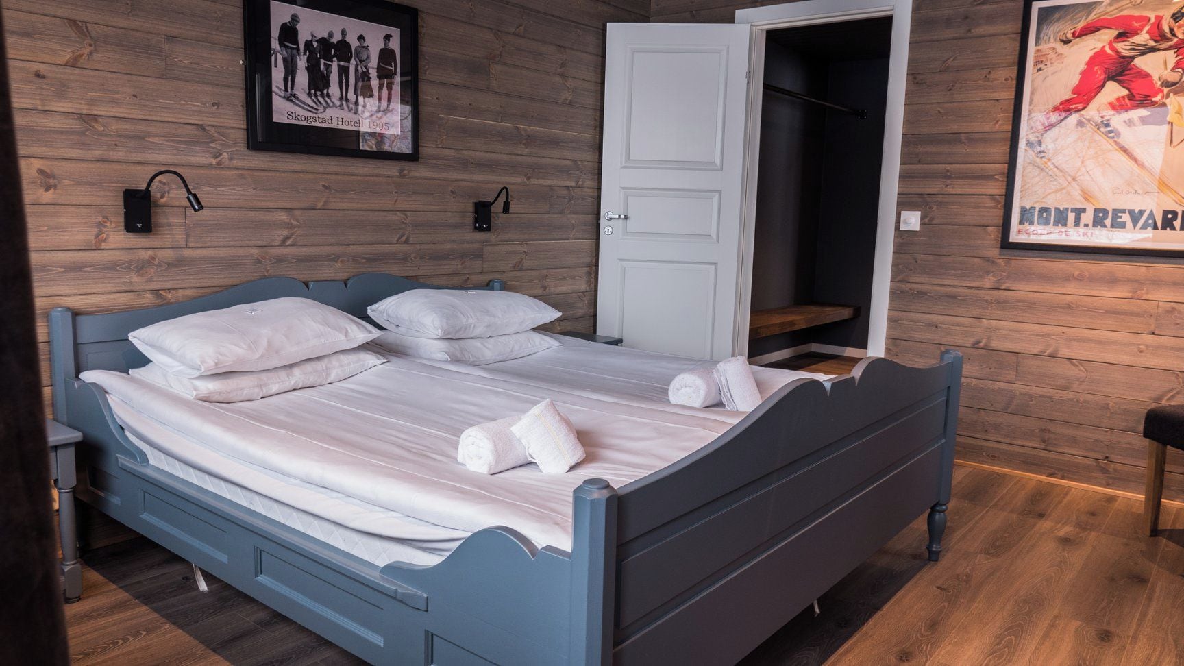 Una cama con ropa blanca y toallas, una pared de madera con un marco y una puerta que da a un armario.