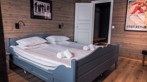 A bed with white linens and towels, a wooden wall with a framed photo, and a door leading to a closet. - Skogstad Hotell - Unike Hoteller (Hemsedal)