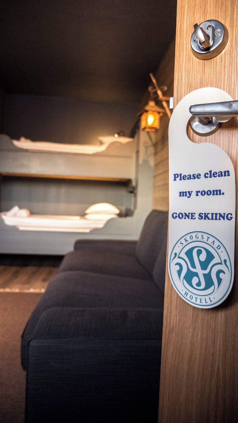 A hotel room with a bunk bed, a wooden door with a metal handle, and a sign requesting guests to clean the room.