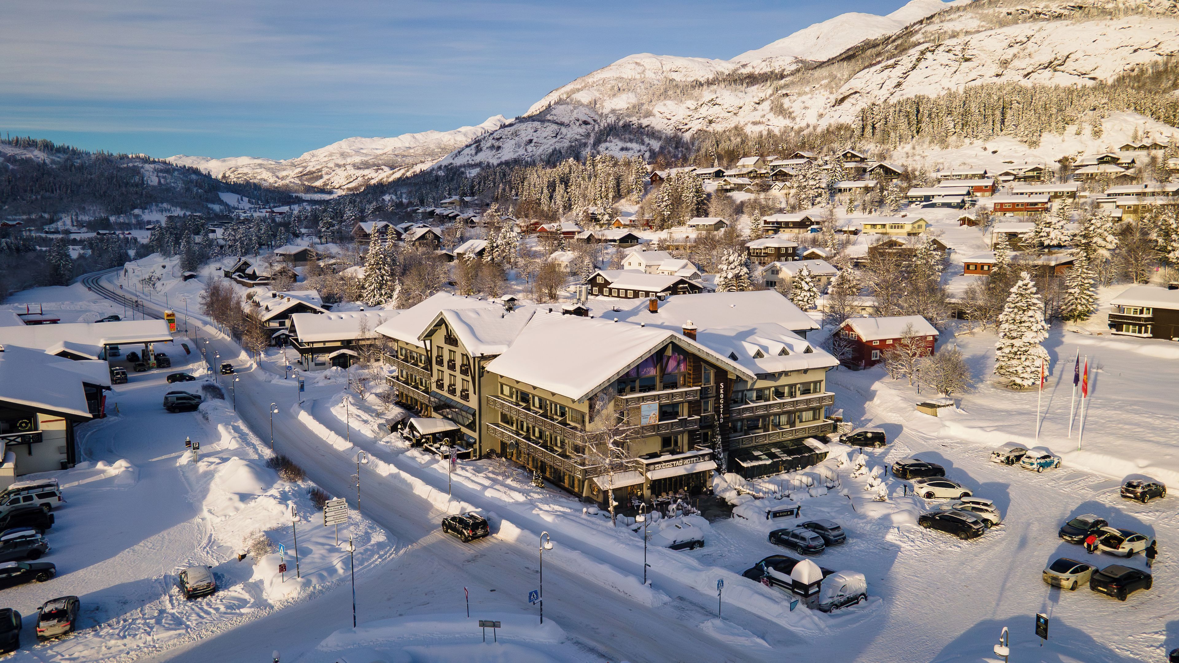 Un pueblo nevado al pie de una montaña, con un hotel destacado que cuenta con un amplio balcón y varios pisos.