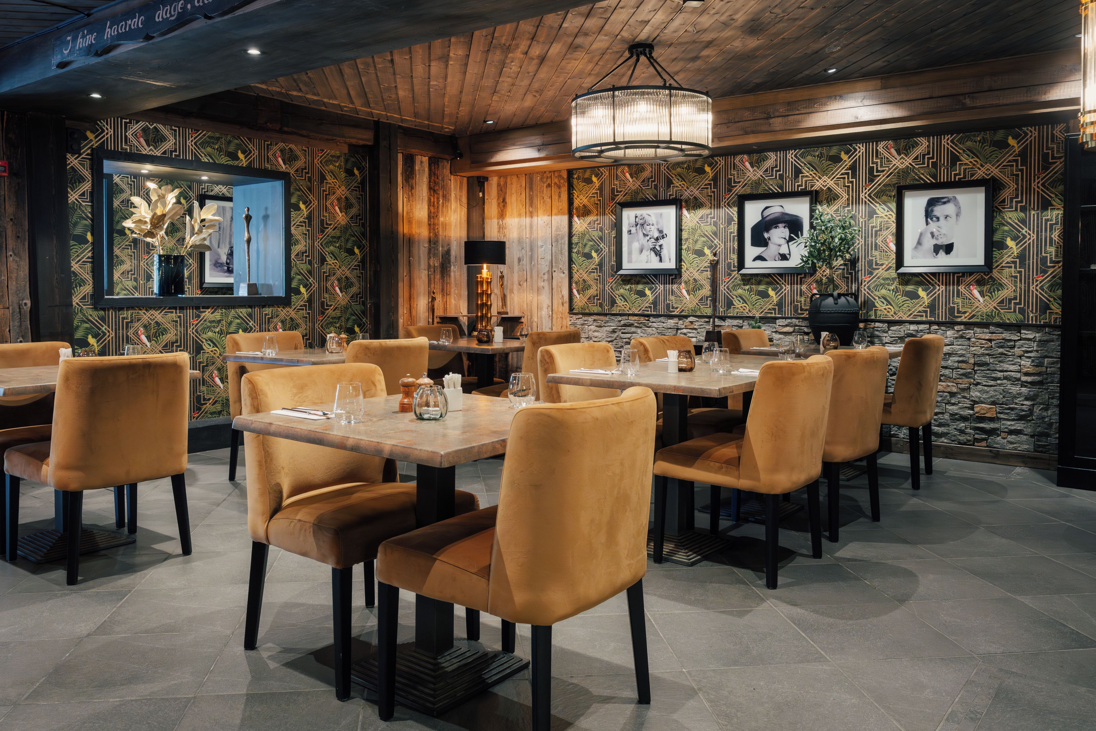 Interior de restaurante con paredes de paneles de madera, obras de arte enmarcadas y un candelabro. Mesas dispuestas con sillas y vajilla.