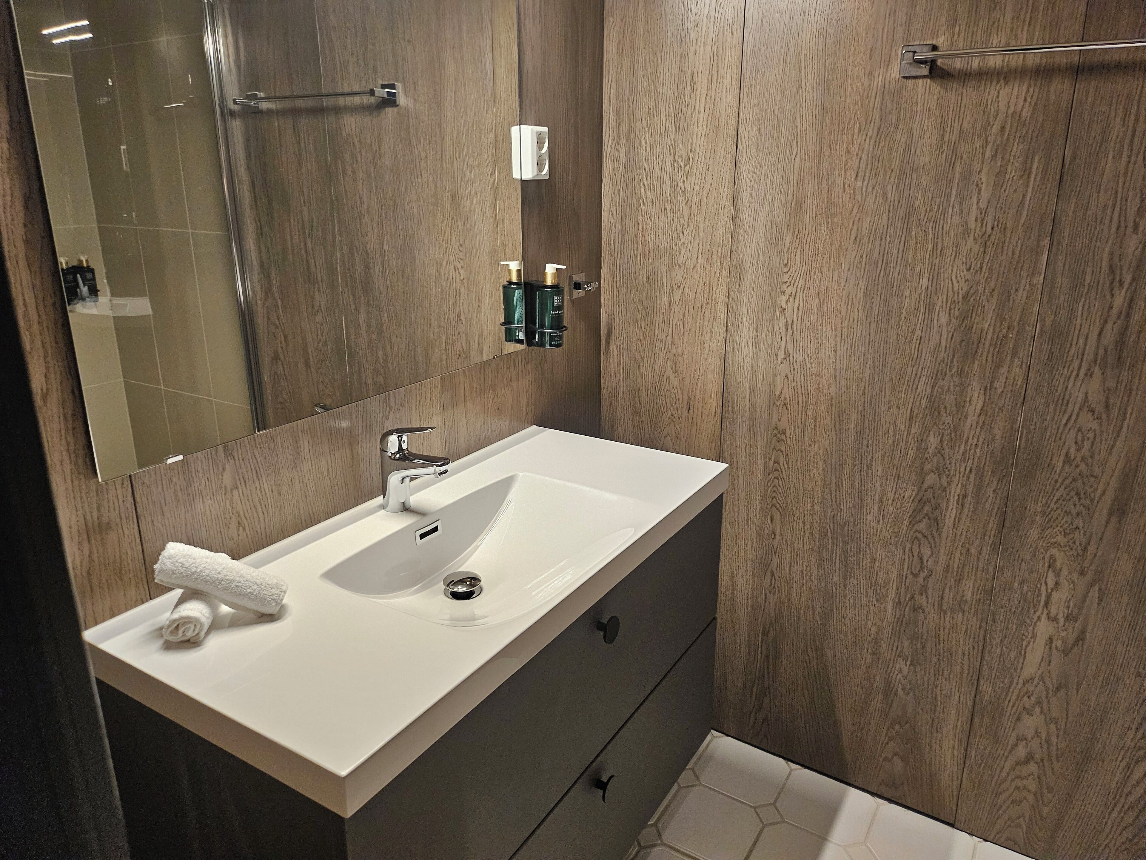 A modern bathroom with a white sink, dark wooden vanity, and a large mirror.