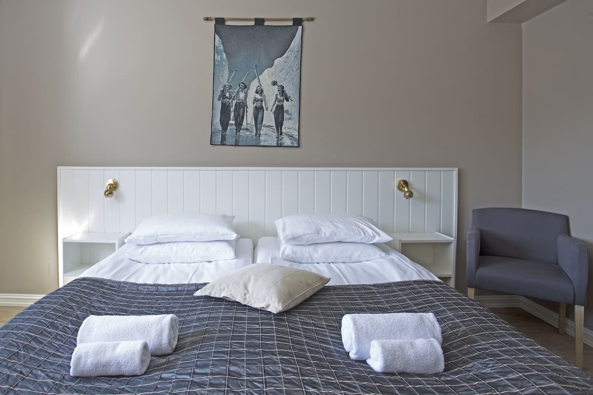 A hotel room with a bed, two nightstands, a chair, and a wall hanging.