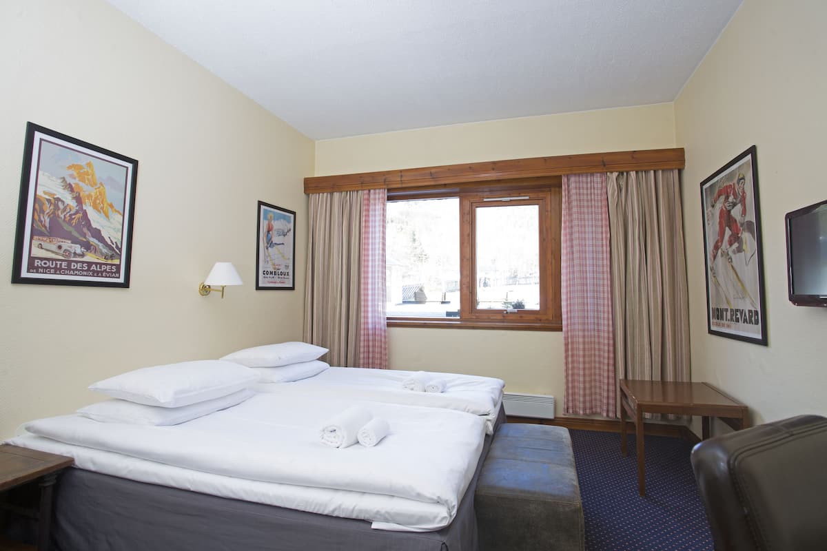 A hotel room with two beds, a small table, a chair, a TV, and curtains.