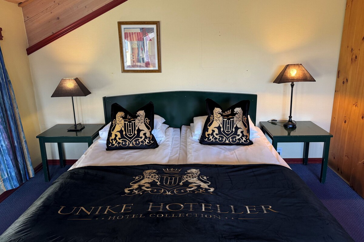 A hotel room with a bed, two nightstands, two lamps, a framed picture on the wall, and a bedspread with the hotel name.