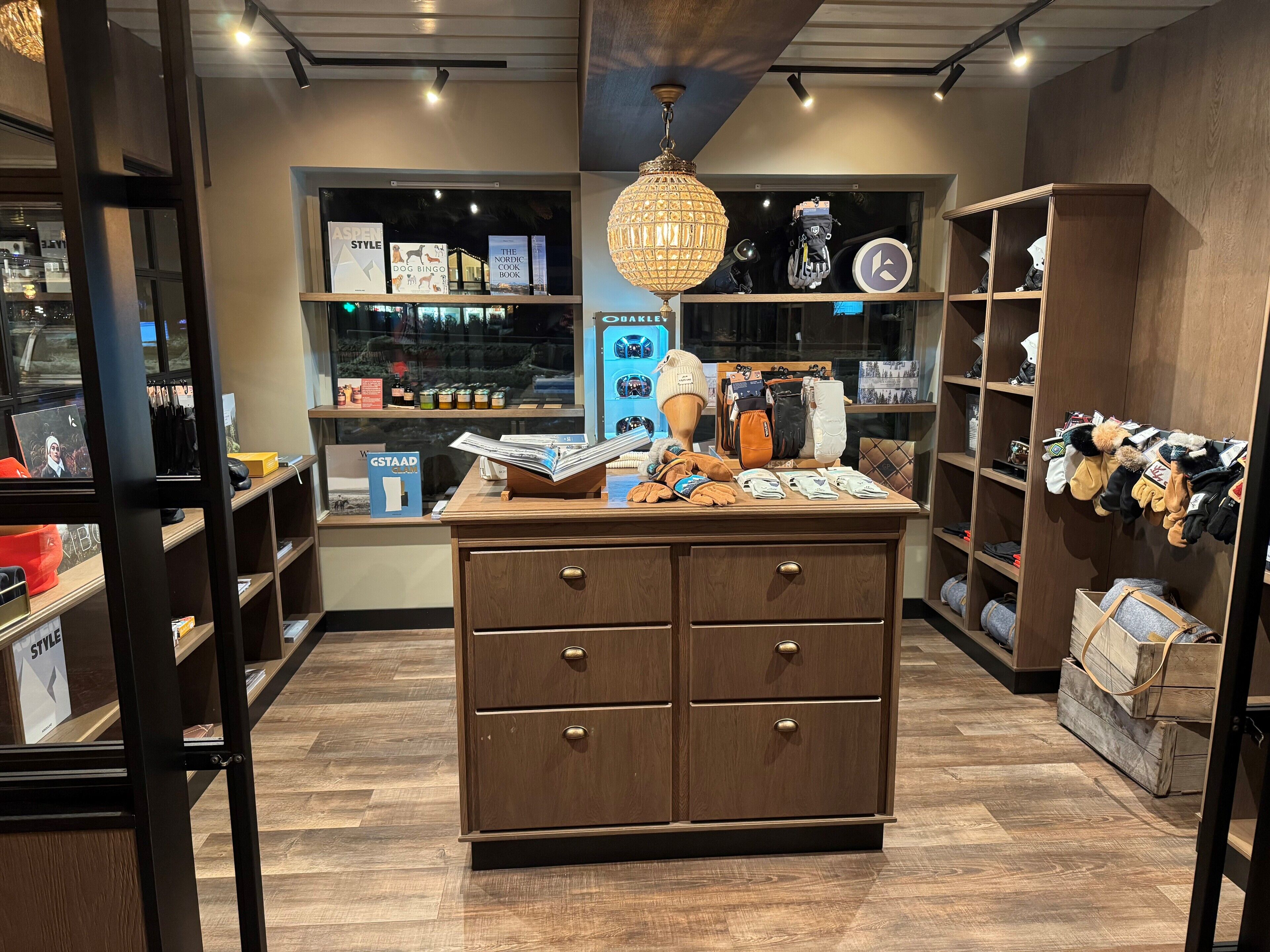 A modern retail store with wooden shelving, a central display table, and a variety of products including books and winter accessories.