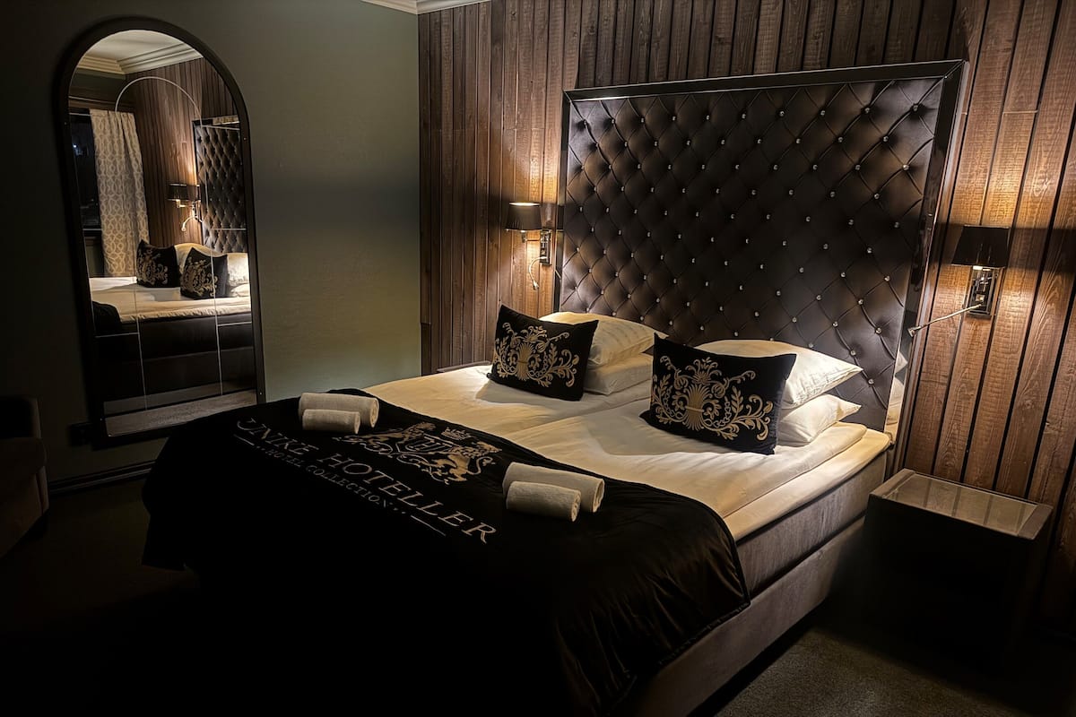 A hotel room with a large bed, a mirror, and wooden paneling on the walls.