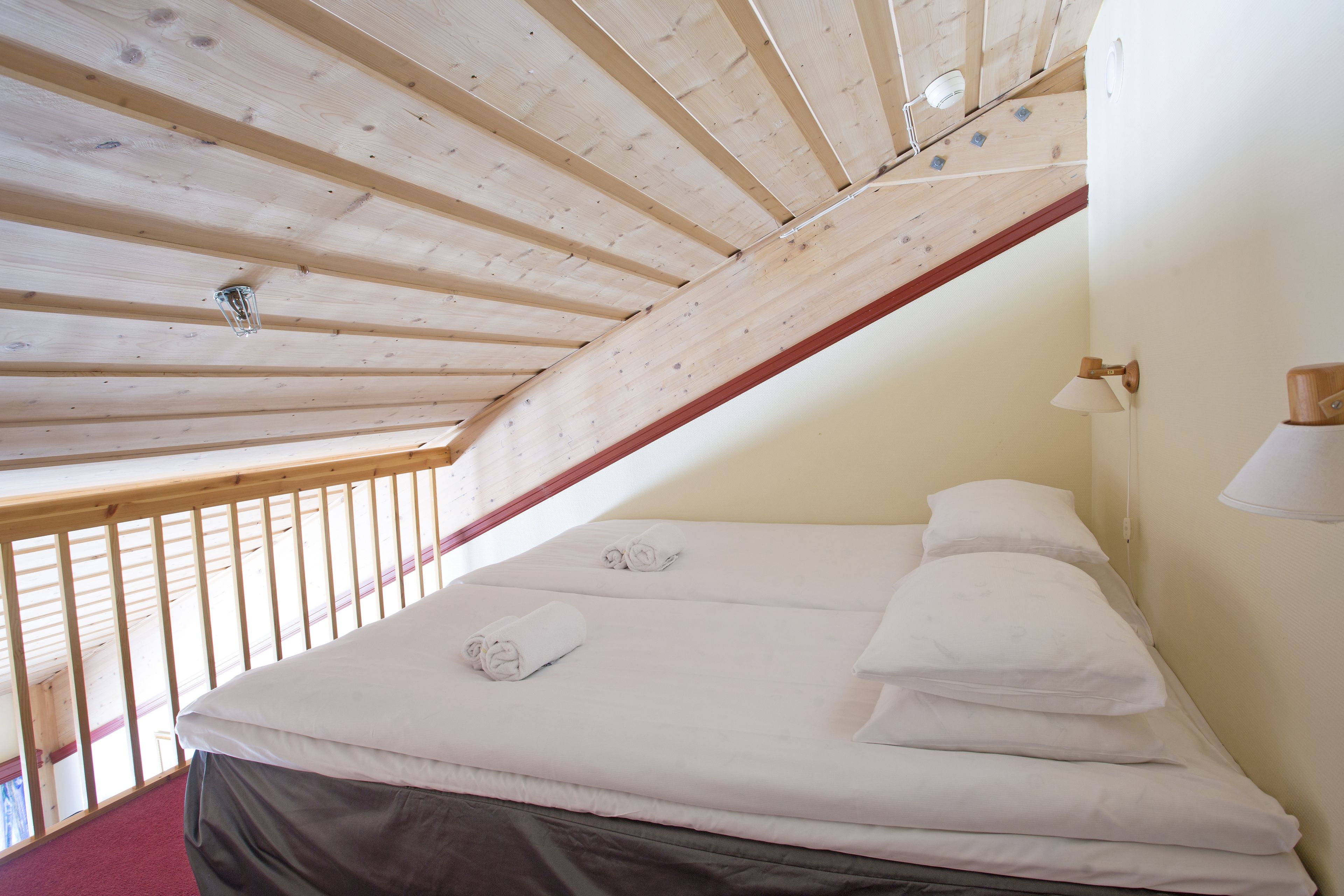 A bedroom with a sloped ceiling, a bed with white linens, and a wooden railing.