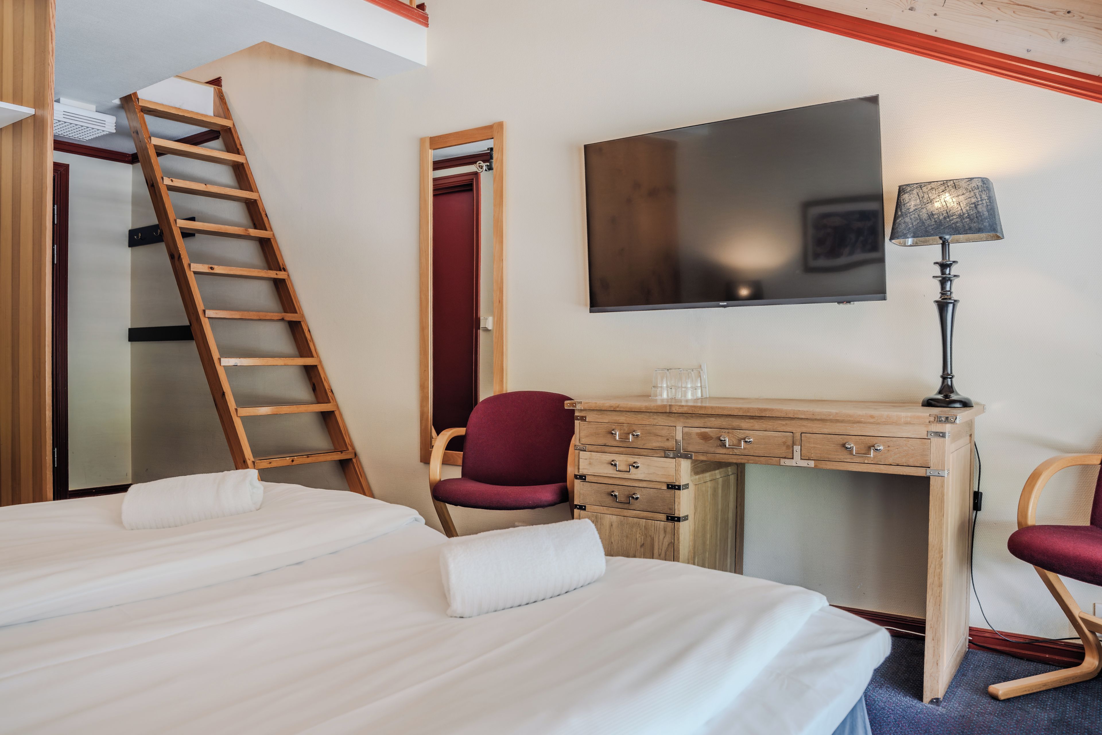 Ein Hotelzimmer mit einem Bett, einem Schreibtisch mit Schubladen, einem Stuhl, einem Fernseher und einer Leiter.
