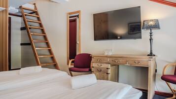 A hotel room with a bed, a desk with drawers, a chair, a TV, and a ladder.