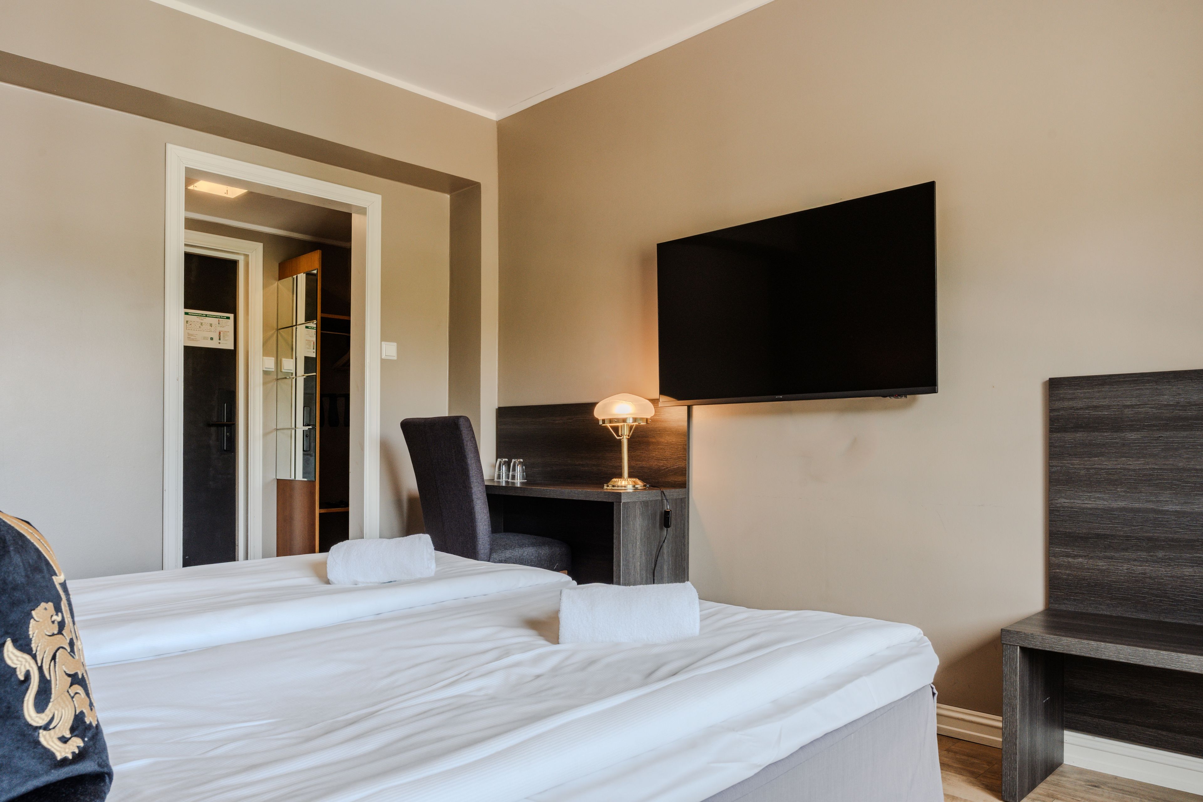 A hotel room with a large bed, a desk, a chair, a television, and a lamp.