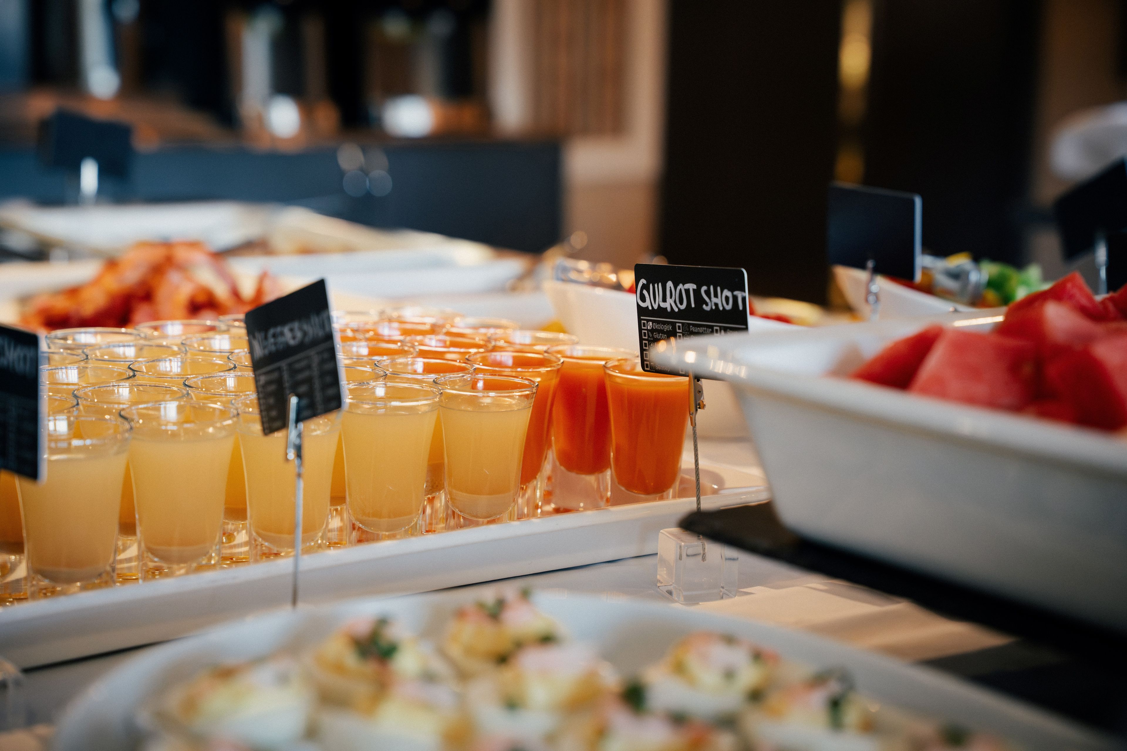 Ein Buffet mit verschiedenen Speisen und Getränken, inklusive einem Schild mit der Aufschrift 'Gulrot Shot'.