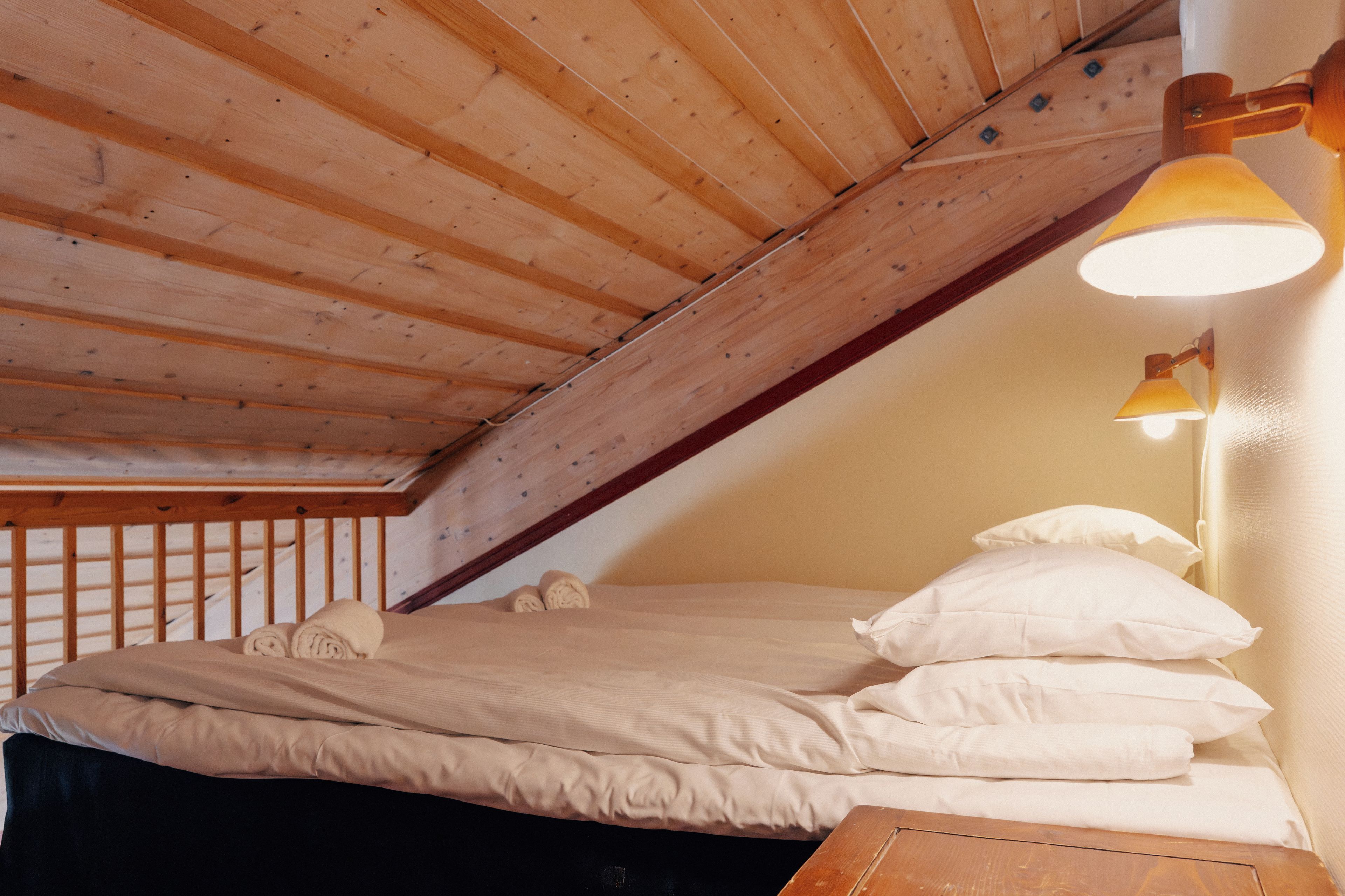 A bedroom with a sloped ceiling, a wooden bed frame, a bedside lamp, and a window.