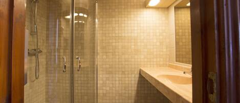A bathroom with a glass-enclosed shower, a beige tiled wall, and a sink with a mirror.