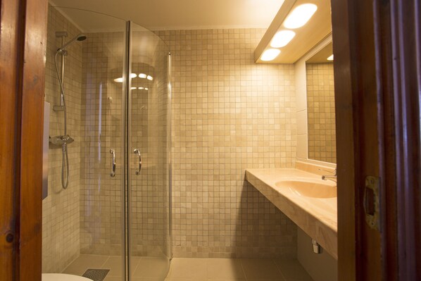 A bathroom with a glass-enclosed shower, a beige tiled wall, and a sink with a mirror.