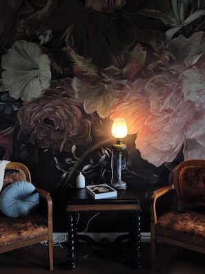 Una habitación con un mural floral, una mesa con una lámpara y dos sillones tapizados.