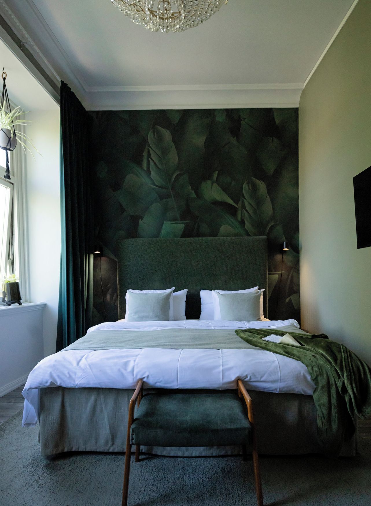 A bedroom with a large bed, a bench, a chandelier, and a wall with a leaf pattern.