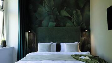 A bedroom with a large bed, a bench, a chandelier, and a wall with a leaf pattern.