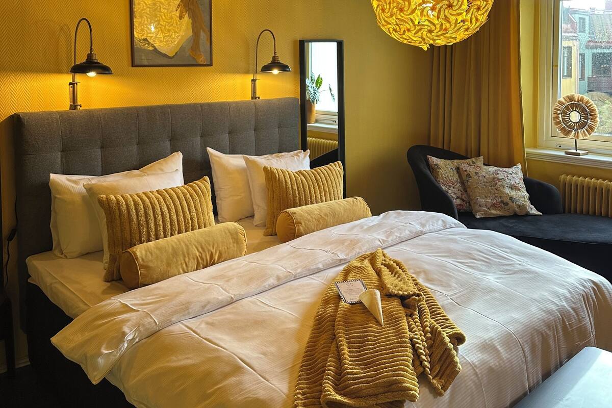 Quarto com uma cama grande, duas luminárias de cabeceira, uma cabeceira e uma janela com cortinas.