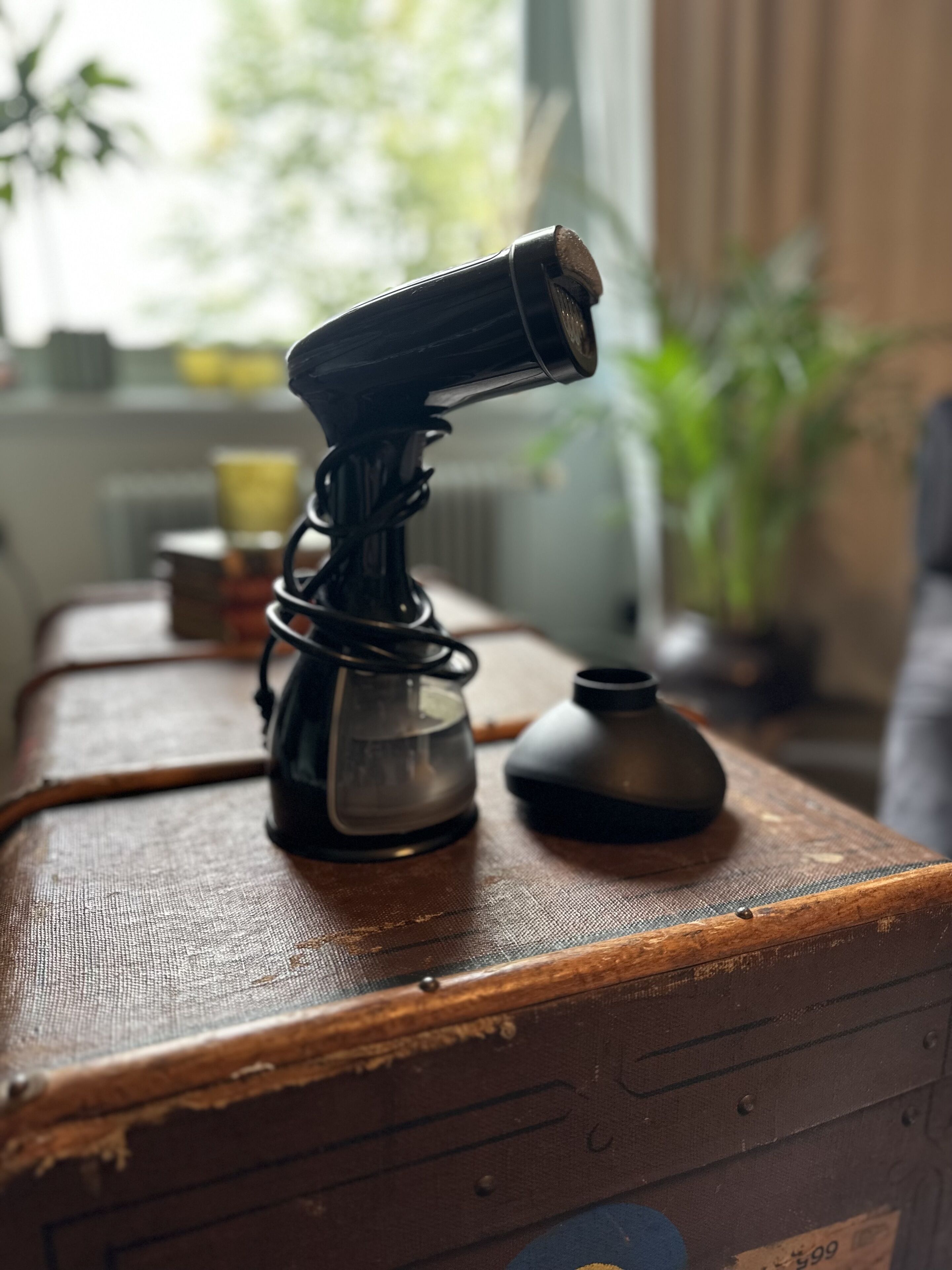 A vintage suitcase with a camera on top, a small kettle, and a vase on a wooden surface.