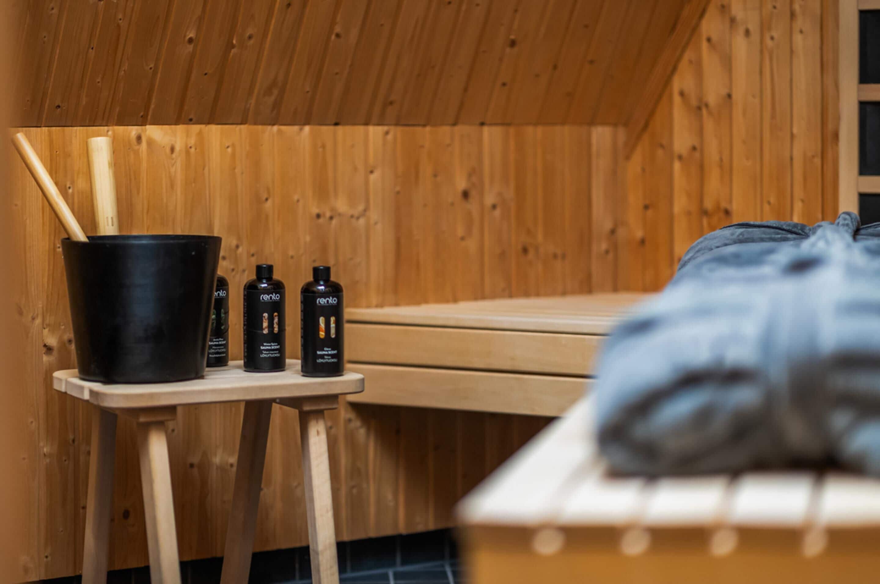 Un sauna avec un banc en bois, un seau et des bouteilles de lotion.