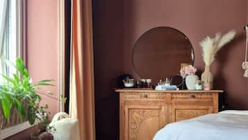 A bedroom with a bed, a dresser, a mirror, a radiator, a window with curtains, and a potted plant.
