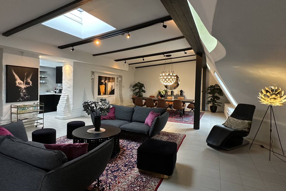 Uma sala de estar moderna com teto alto, claraboia e área de jantar com lustre.