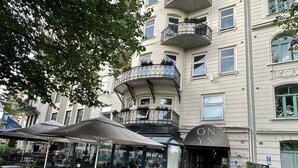 Un edificio de varios pisos con balcones, mobiliario exterior y una zona de café.