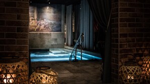 Zona de spa tenuemente iluminada, con pared de piedra, piscina iluminada en azul y lámparas de mimbre.
