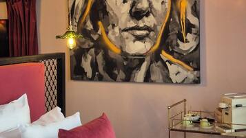 A bedroom with a bed, pillows, a bedside table with a lamp, and a wall-mounted painting.