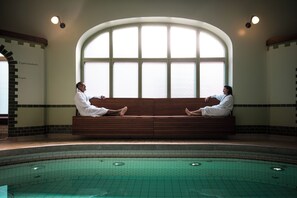 Dos personas sentadas en un banco junto a un ventanal con vistas a una piscina.