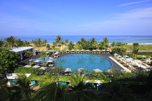 Un resort con una amplia piscina circular rodeada de sillas de descanso y sombrillas, palmeras y vistas al océano.