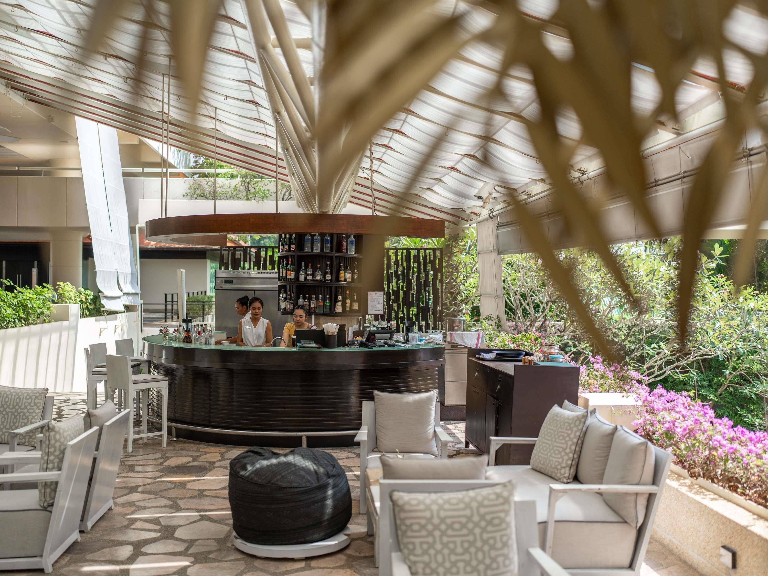 Zona de bar al aire libre con asientos, una barra con personal de bar y vistas a zonas verdes.