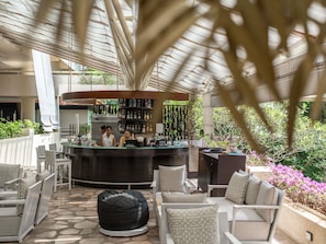 An outdoor bar area with seating, a counter with bar staff, and a view of greenery. - Pullman Phuket Karon Beach Resort (Karon)