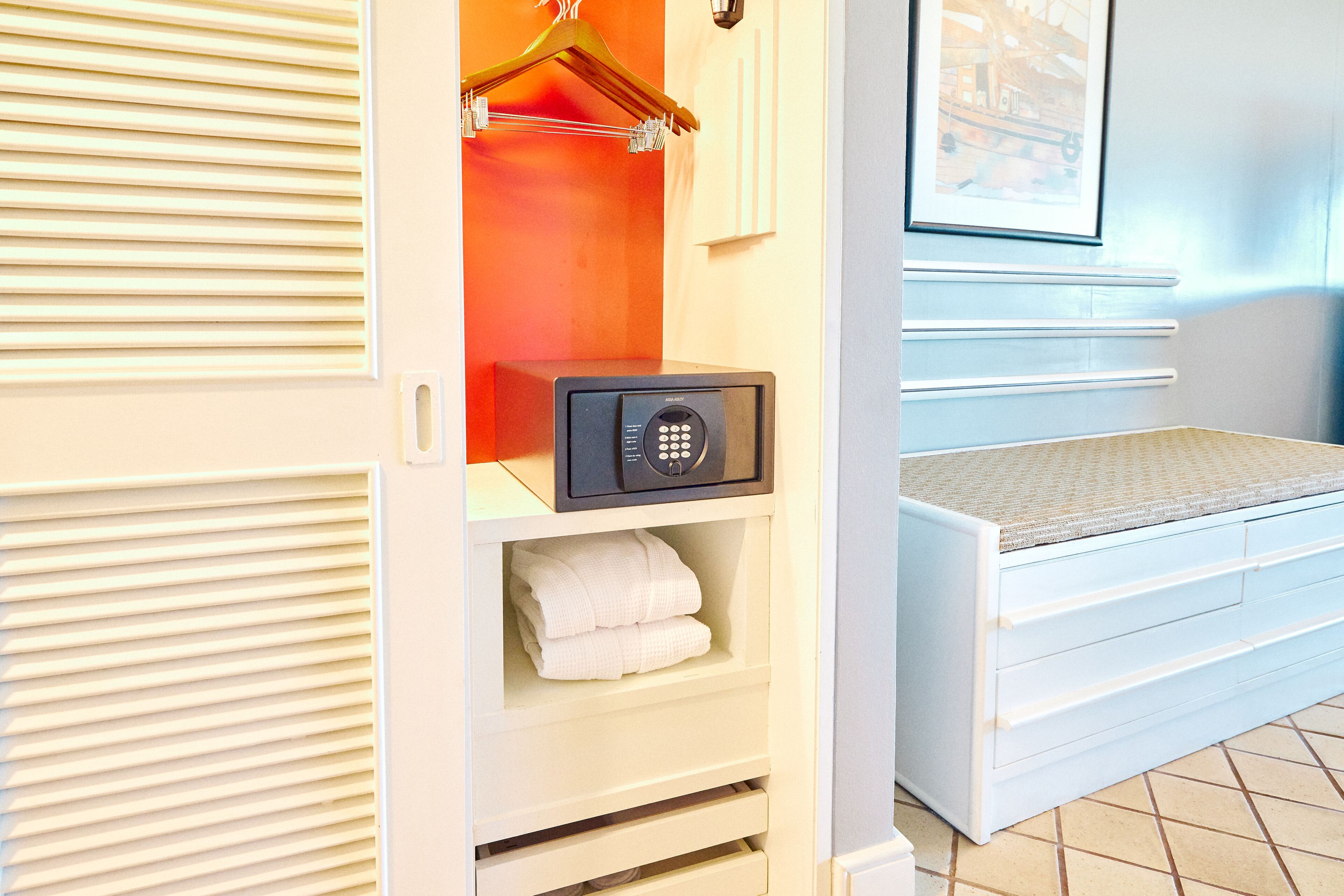 Una habitación de hotel con vestidor, caja fuerte y cama con cabecera.
