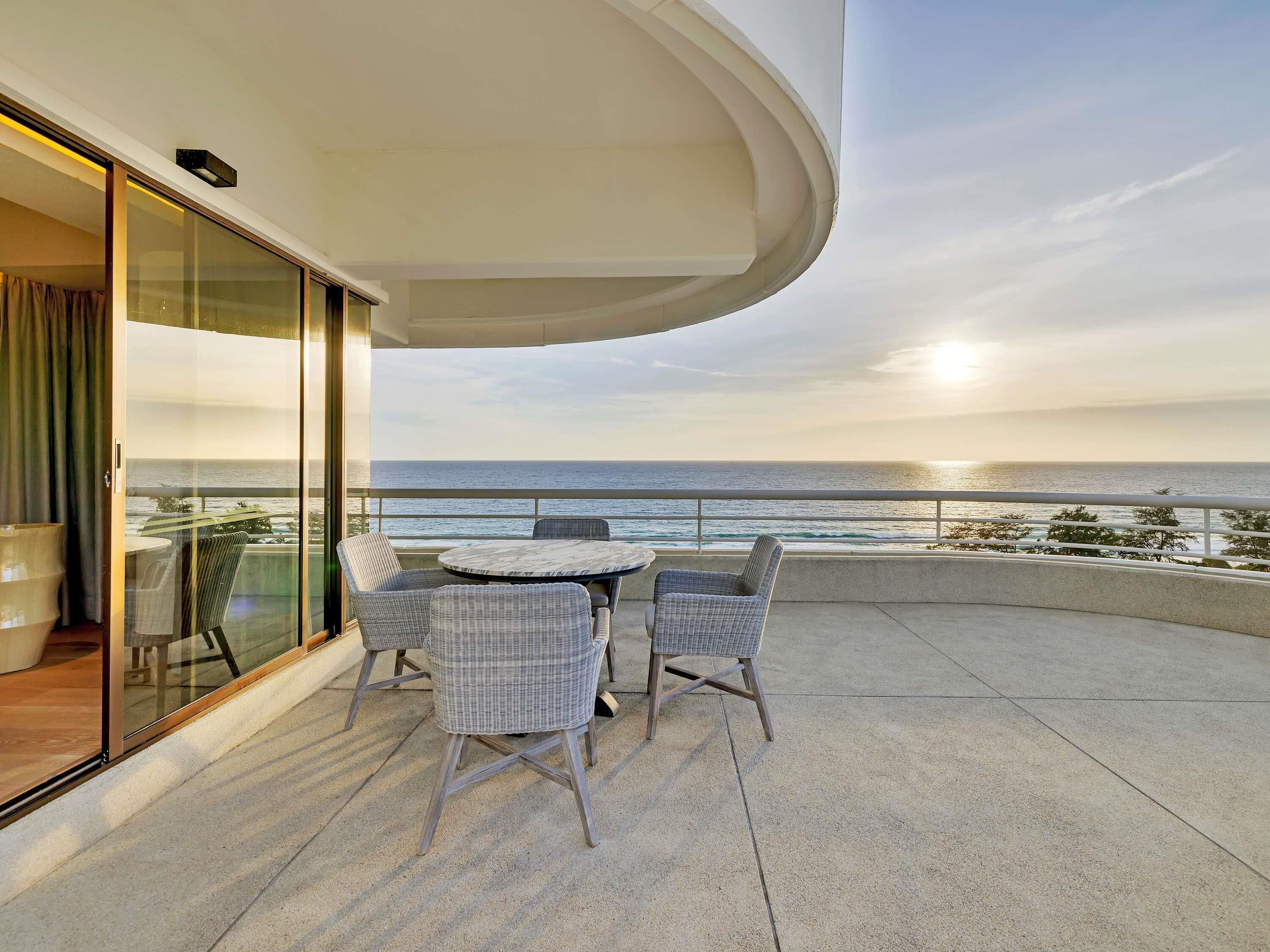 A balcony with a table and chairs, a glass door, and a view of the ocean.