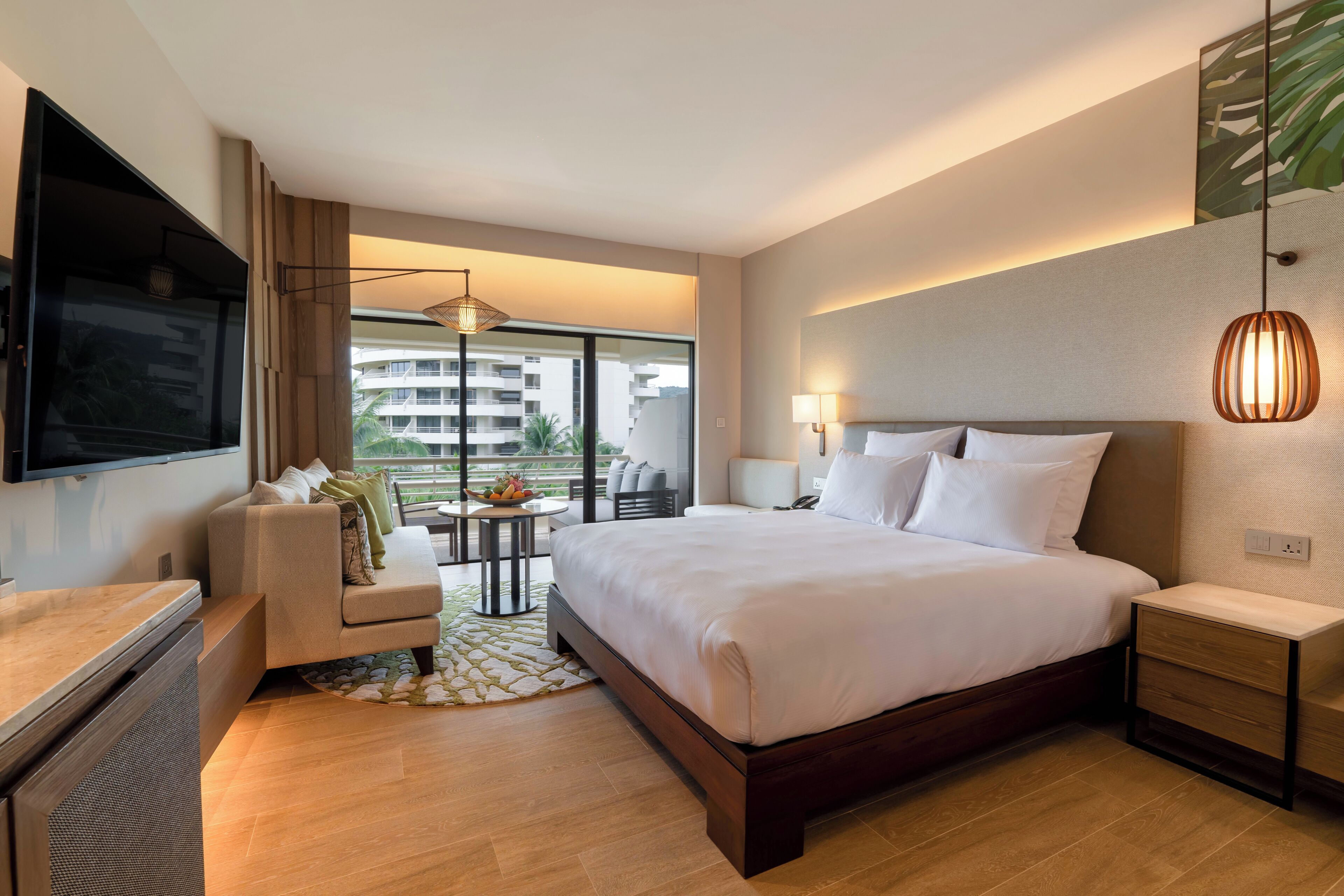 Une chambre d’hôtel moderne dotée d’un grand lit, d’un téléviseur fixé au mur, d’un coin salon avec une table et offrant une vue sur la ville grâce à de grandes fenêtres.