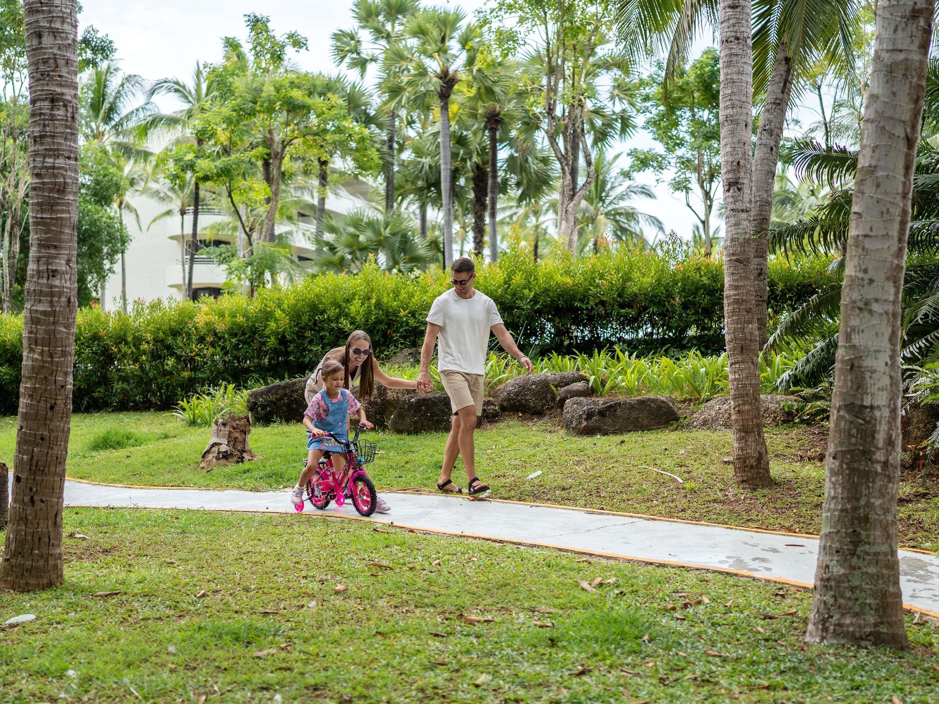 A pathway in a lush, green outdoor area with palm trees and a building in the background.