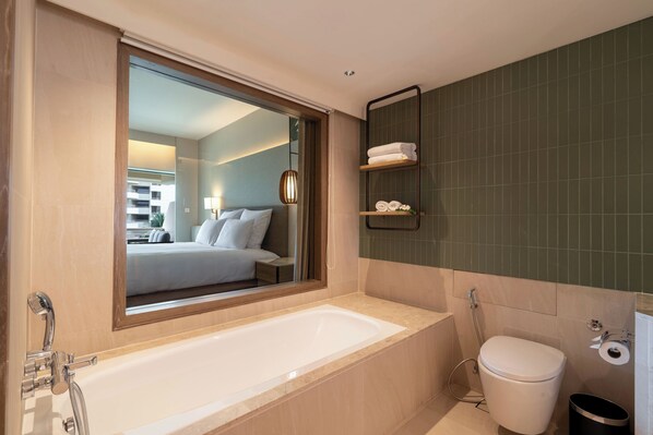 A modern bathroom with a large bathtub, a toilet, and a mirror reflecting a bedroom. - Pullman Phuket Karon Beach Resort (Karon)