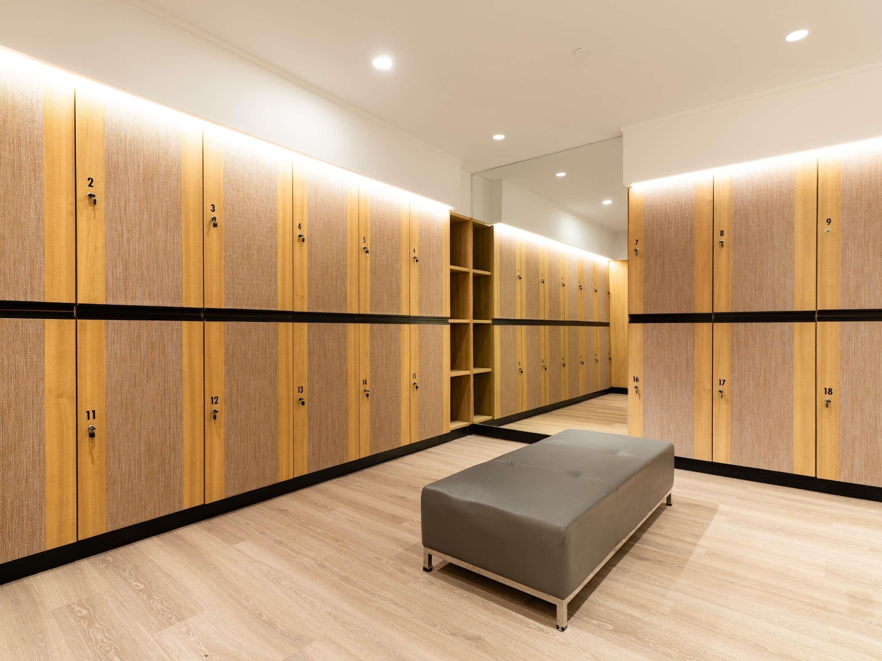 Un vestuario moderno con taquillas de madera, un banco y un muro con espejos.