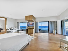 Una habitación de hotel moderna con una cama grande, televisión y balcón con vistas al mar.