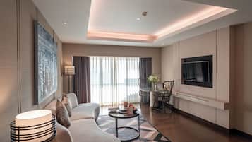 A modern living room with a sofa, a coffee table, a TV, and a large window with curtains.