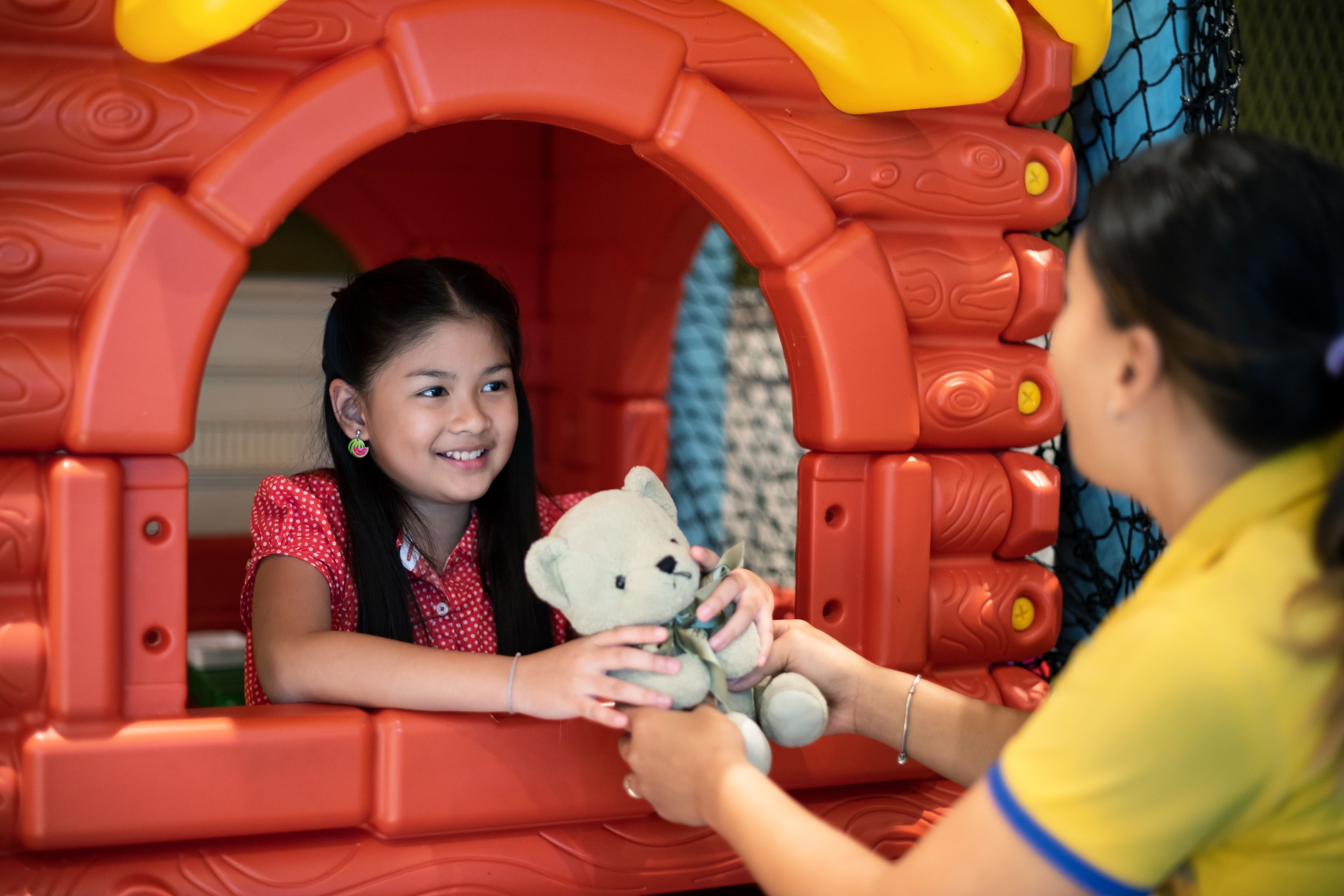 Un enfant tenant un ours en peluche à l’intérieur d’une structure de jeu.