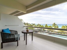 A balcony with a view of the ocean, a chair, a small table, and a towel rack.