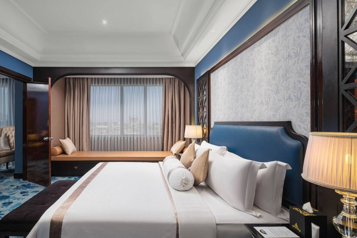 A hotel room with a large bed, a sofa bed, a television, and a view of the city through the window.