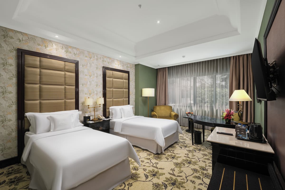 A hotel room with two beds, a desk with a lamp, a chair, and a television.