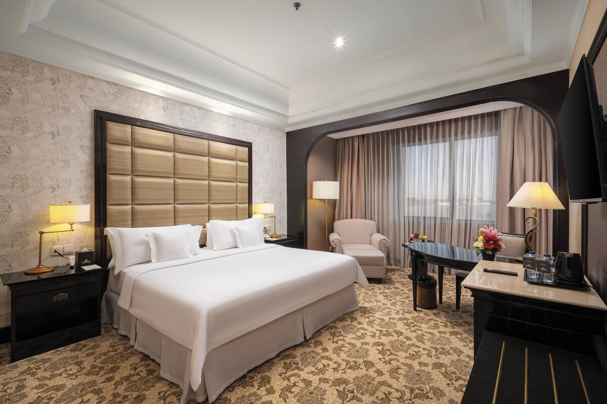 A hotel room with a large bed, a desk with a chair, a TV, and a window with curtains.