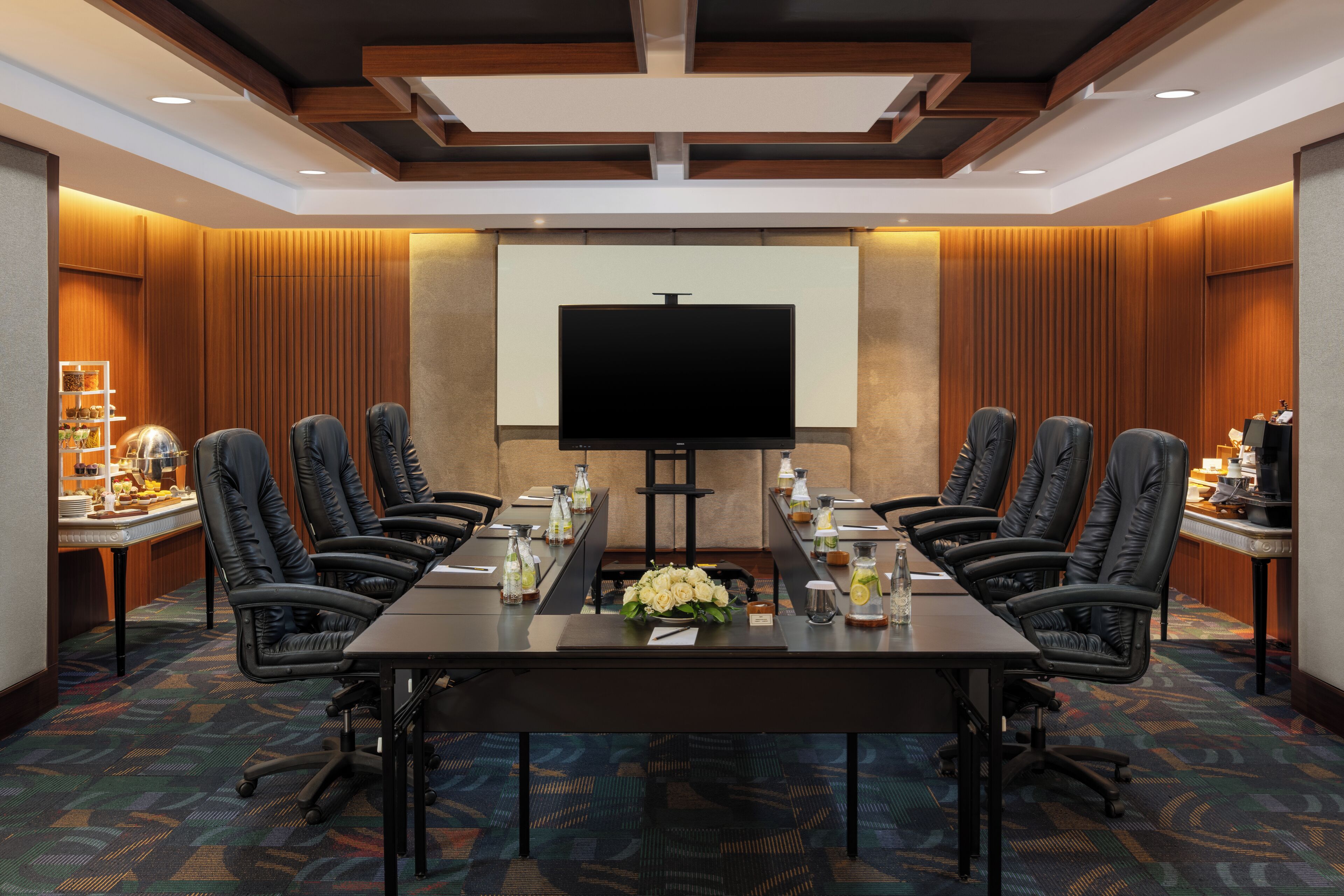 A conference room with a large table, chairs, a projector screen, and a floral centerpiece.
