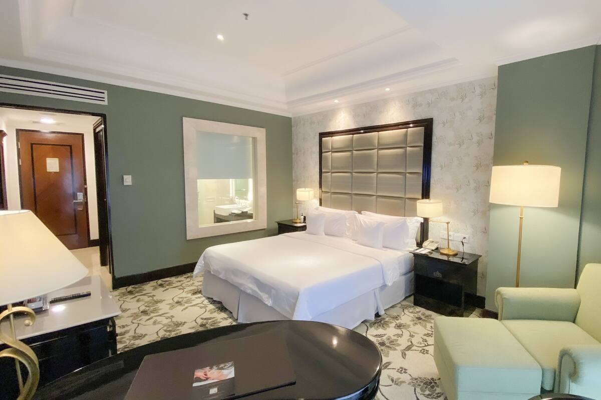 A hotel room with a bed, two bedside tables with lamps, a chair, a mirror, and a door.