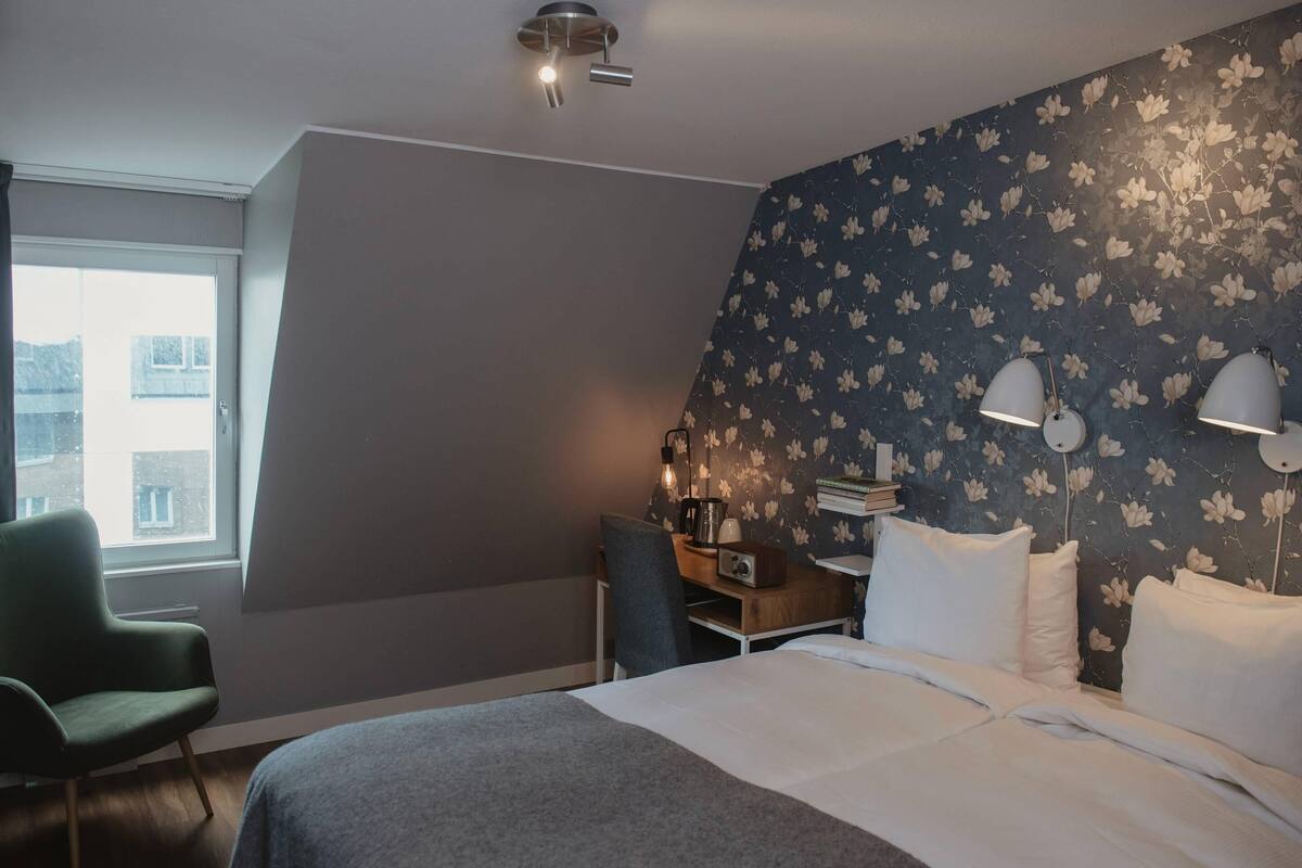 A hotel room with a bed, a desk, a chair, and a window.
